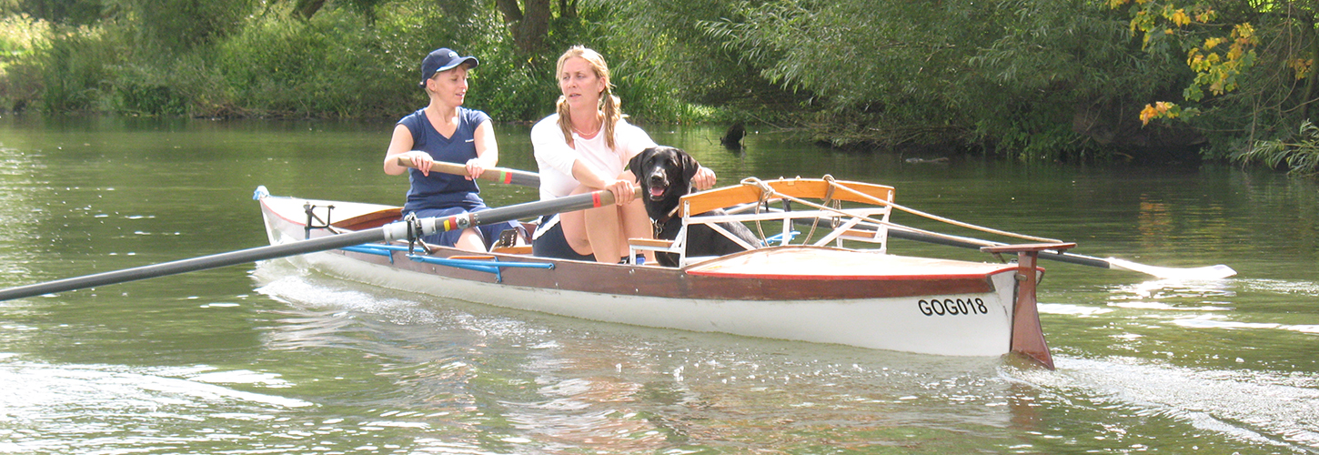 2 rowers in wide boat with dog