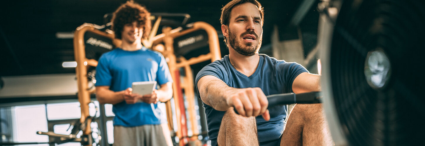 Rower with personal trainer on indoor machine at gym