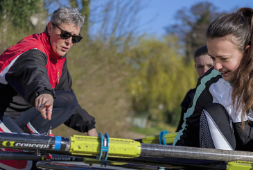 Coach helping 2 new rowers on landing stage