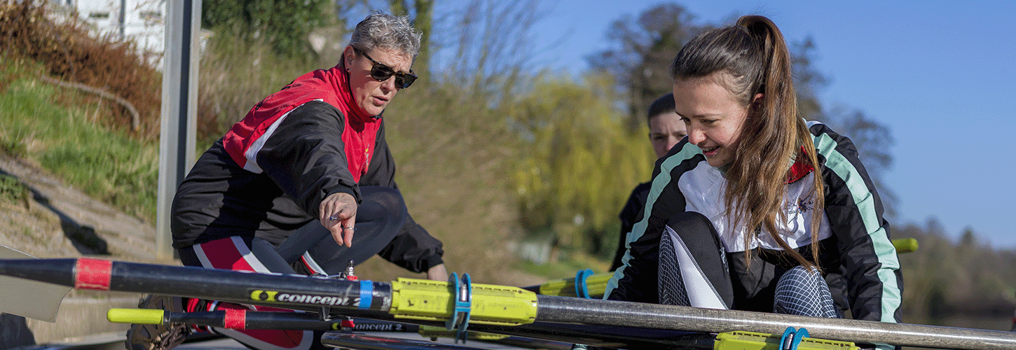 Coach helping 2 new rowers on landing stage